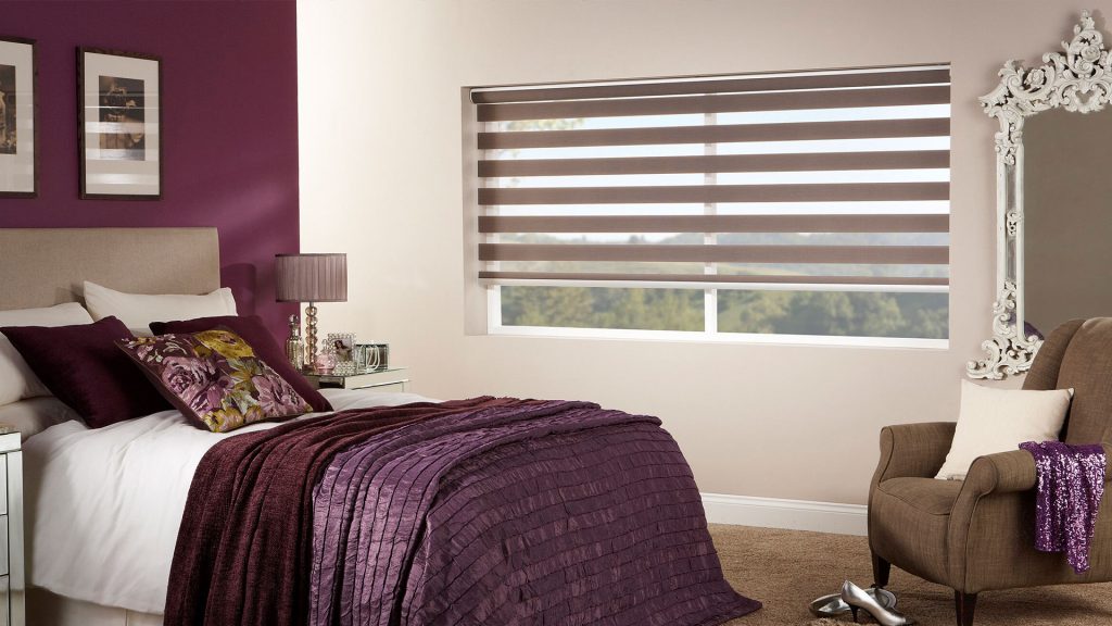 Vision blinds with alternating opaque and sheer brown stripes in a stylish bedroom.